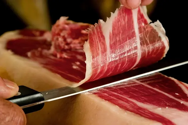 Slicing cured ham and salami on wooden board for charcuterie category