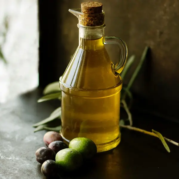 Glass bottle of extra virgin olive oil with fresh olives and leaves