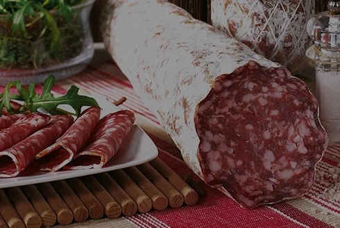 Sliced dry sausage and saucisson on a charcuterie board with herbs