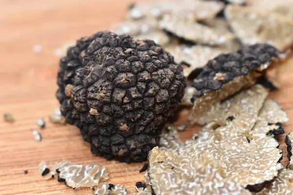 Whole black truffles and sliced truffle on a wooden board with rice